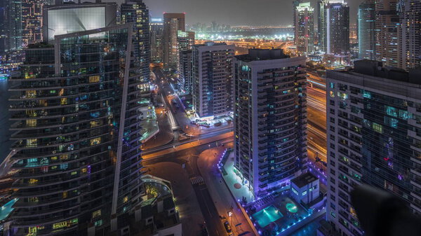 View of various skyscrapers and towers in Dubai Marina from above aerial night timelapse. Illuminated modern buildings in urban skyline with traffic on streets