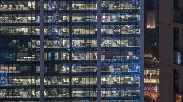 Office building exterior during late evening with interior lights on and people working inside night timelapse