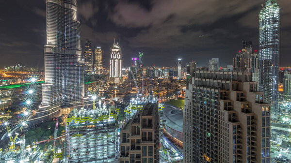 Panoramic skyline view of Dubai downtown with mall, fountains and Burj Khalifa aerial timelapse during all night with lights swithcing off. Modern illuminated skyscrapers and construction site
