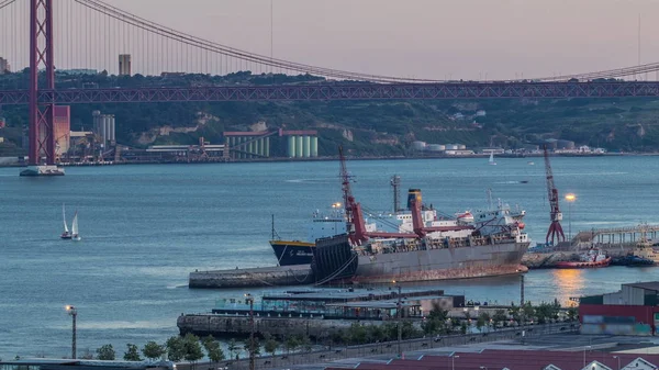 Skyline πάνω από το εμπορικό λιμάνι της Λισαβόνας μέρα με τη νύχτα timelapse, 25 Απριλίου Γέφυρα, εμπορευματοκιβώτια στην προβλήτα με γερανούς εμπορευμάτων — Φωτογραφία Αρχείου