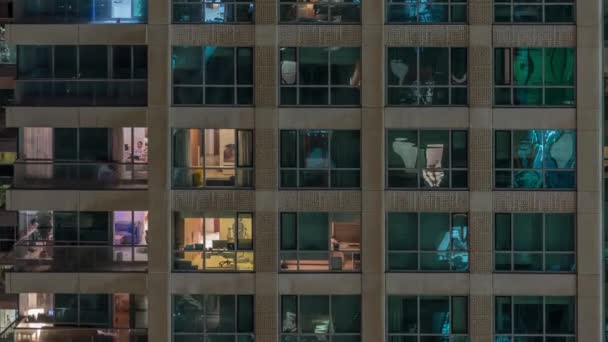 Janelas do edifício de vários andares com iluminação interior e pessoas em movimento em apartamentos timelapse . — Vídeo de Stock
