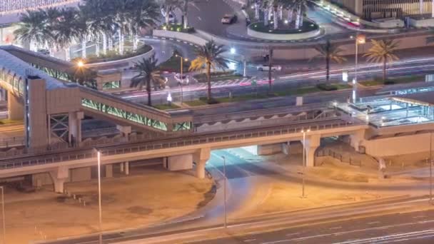 Bovenaanzicht van het verkeer in de buurt van het winkelcentrum met voetgangersbrug van tramhalte 's nachts timelapse in Dubai Marina in Dubai, VAE. — Stockvideo