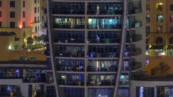 Filas de ventanas brillantes con gente en el edificio de apartamentos por la noche . — Vídeo de stock