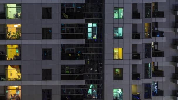 Filas de ventanas brillantes con gente en el edificio de apartamentos por la noche . — Vídeo de stock