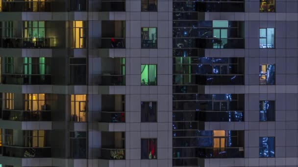 Filas de ventanas brillantes con gente en el edificio de apartamentos por la noche . — Vídeo de stock
