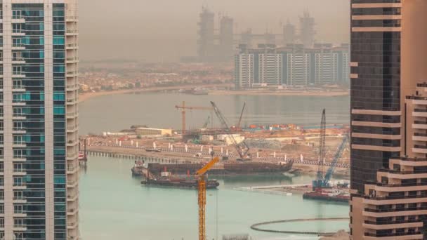 Vista aérea de los rascacielos del puerto deportivo de Dubái con obras de construcción y Palm Jumeirah Island en el timelapse de fondo . — Vídeos de Stock