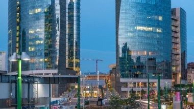 Milan Porta Nuova iş bölgesi gün gece geçiş timelapse Milan, İtalya, güneş battıktan sonra içinde modern gökdelenler ile manzarası. Yolda trafik. Işık içinde pencere eşiği. Köprüsü'nden Üstten Görünüm