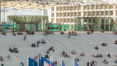 Merdivenleri olan Büyük Kemer ve üzerinde oturan insanlar Fransa, Paris 'in Savunma İş Bölgesi' nde zamanlarını ayarlıyorlar. Yaz günü mavi bulutlu bir gökyüzü. Üst görünüm