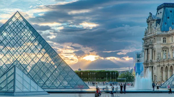 日没時のルーヴル美術館のピラミッドは フランスのパリで経過する 夏の日にカラフルな空 噴水の近くの広場を歩く人々 — ストック写真