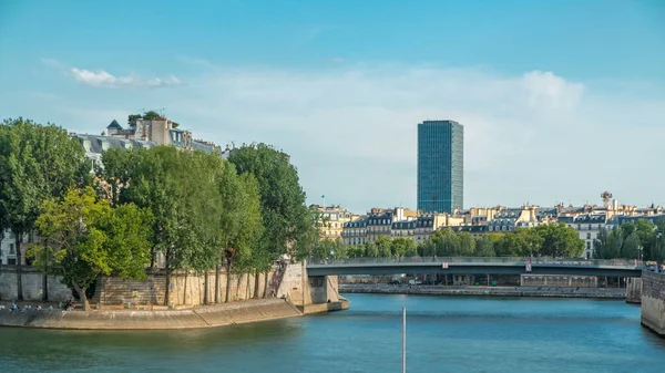 Embankment of the river Seine near Notre Dame with Saint-Louis bridge timelapse before sunset. View of the houses and trees of the island of Saint-Louis.