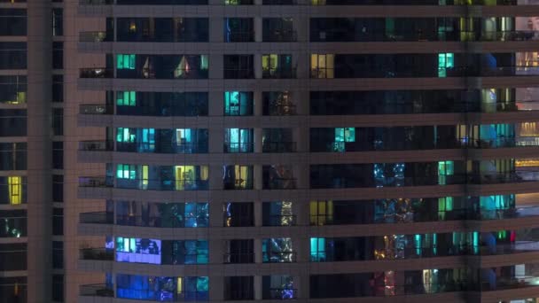 Filas de ventanas brillantes con gente en el edificio de apartamentos por la noche . — Vídeo de stock