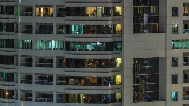 Rows of glowing windows with people in apartment building at night. — Stock Video