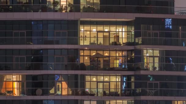 Filas de ventanas brillantes con gente en el edificio de apartamentos por la noche . — Vídeos de Stock