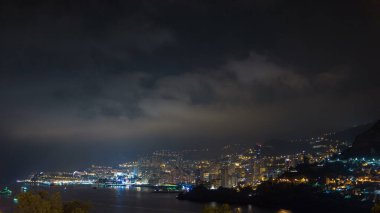 Monte Carlo 'nun şehir manzarası, Monaco, gece vakti. Akşam sisi bulutlara dönüşür. Binaların gece aydınlanması. Limandaki yatlar. Kaptan Martin 'den üst görünüm