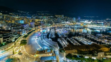 Monte Carlo 'nun Panorama' sı geceleyin Herkül Limanı ile Monako köyündeki gözlem güvertesinden. Liman manzaralı, aydınlık binalar ve yatlar. Trafik vardı.