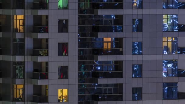 Filas de ventanas brillantes con gente en el edificio de apartamentos por la noche . — Vídeo de stock