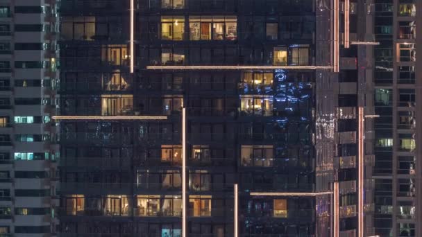 Filas de ventanas brillantes con gente en el edificio de apartamentos por la noche . — Vídeo de stock