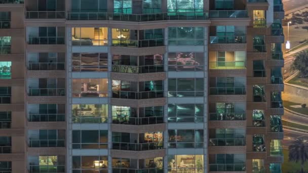 Rows of glowing windows with people in apartment building at night. — Stock Video