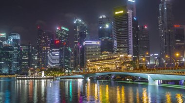 Esplanade Köprüsü ve şehir merkezindeki gökdelenler arka planda Singapur 'da gece vakti hızlandırılmış. Aydınlatılmış kuleler suya yansıyor
