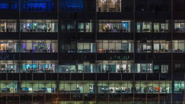Gece vakti büyük pencereleri olan modern ofis binası yakın çekim manzarası, parlayan pencereler ve Singapur 'daki bazı insanlar. Uzaklaştır