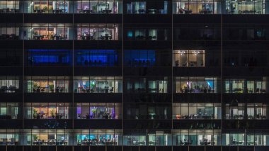 Gece vakti büyük pencereleri olan modern ofis binası yakın çekim manzarası, parlayan pencereler ve Singapur 'daki bazı insanlar. Yakınlaştır