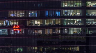 Gece vakti büyük pencereleri olan modern ofis binası yakın çekim manzarası, parlayan pencereler ve Singapur 'daki bazı insanlar. Sola çevir