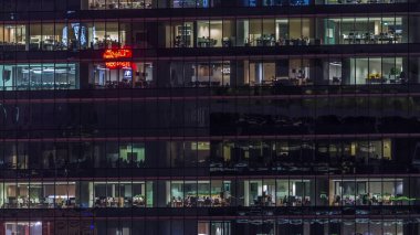 Gece vakti büyük pencereleri olan modern ofis binası. Yakın görüş, parlayan pencereler ve Singapur 'da yaşayan bazı insanlar.