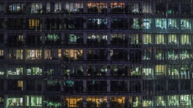 Gece vakti büyük pencereleri olan modern ofis binası yakın çekim manzarası, parlayan pencereler ve Singapur 'daki bazı insanlar. Sola çevir