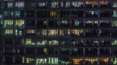 Gece vakti büyük pencereleri olan modern ofis binası. Yakın görüş, parlayan pencereler ve Singapur 'da yaşayan bazı insanlar.