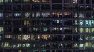 Gece vakti büyük pencereleri olan modern ofis binası. Yakın görüş, parlayan pencereler ve Singapur 'da yaşayan bazı insanlar.