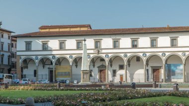 Santa Maria Novella Meydanı zaman çizelgesi. Floransa 'nın en önemli meydanlarından biri. Çiçek yatakları ve yeşil çimenler. İnsanlar bankta oturuyor. Yazın mavi gökyüzü