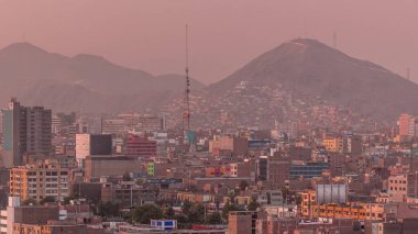 Gün batımında Lima şehrinin panoramik ufuk çizgisi ve birçok binanın havadan zaman çizelgesi. Arka planda tepeler olan fakir evler. Sokakta trafik vardı. Lima, Peru