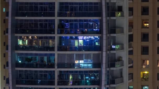 Filas de ventanas brillantes con gente en el edificio de apartamentos por la noche . — Vídeo de stock