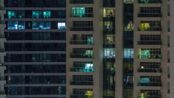 Rijen van gloeiende ramen met mensen in appartementencomplex 's nachts. — Stockvideo