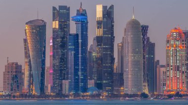 Doha şehir merkezi ufuk çizgisi günden geceye geçiş zamanı, Katar, Orta Doğu. Batı Körfezi 'ndeki aydınlık gökdelenler Körfez suyuna yansıyor.