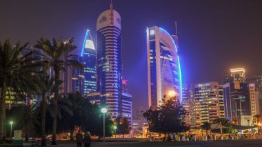 Doha 'nın yüksek katlı bölgesinde gece vardiyası, parktan görülmüş. Batı körfezinde aydınlatılmış gökdelenler ve palmiyeler