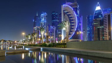 Geceleri Doha 'nın ufuk çizgisi. Yıldızlı gökyüzü Park Timelapse, Katar' dan görülüyor. Aydınlatılmış gökdelenler ve kuleler çeşme suyuna yansıyor