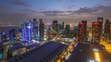 Batı Körfezi bölgesinin ufuk çizgisi Doha 'da günden geceye geçiş zamanı, Katar. Günbatımından sonra modern gökdelenlerin çatıdan görünüşü aydınlandı. Yolda trafik vardı.