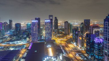 Katar 'ın Doha Zaman Çizelgesi' nde Batı Körfezi bölgesinin ufuk çizgisi. Aydınlatılmış modern gökdelenler geceleri çatıdan gökyüzü manzarası. Yolda trafik vardı.