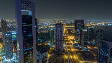 Katar 'ın Doha Zaman Çizelgesi' nde Batı Körfezi bölgesinin ufuk çizgisi. Aydınlatılmış modern gökdelenler geceleri çatıdan gökyüzü manzarası. Yolda trafik vardı.