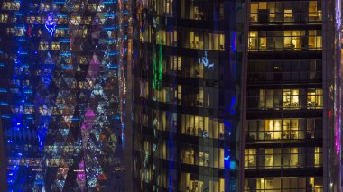 İçerideki cam ve çelik ofis aydınlatması ve çalışan insanların çok katlı binasının zaman çizelgesi. Gökdelenlerin gece aydınlanması. Doha, Katar