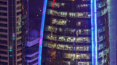 İçerideki cam ve çelik ofis aydınlatması ve çalışan insanların çok katlı binasının zaman çizelgesi. Gökdelenlerin gece aydınlanması. Doha, Katar