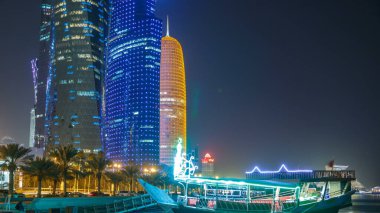 Geleneksel dhow botu Doha 'da, arka planında modern binalar olan gece zaman diliminde. Batı körfezinde aydınlık gökdelenler.
