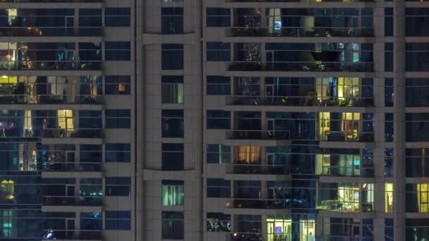 Filas de ventanas brillantes con gente en el edificio de apartamentos por la noche . — Vídeo de stock