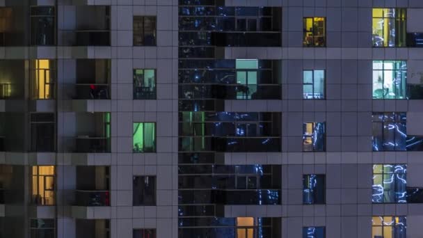 Filas de ventanas brillantes con gente en el edificio de apartamentos por la noche . — Vídeo de stock