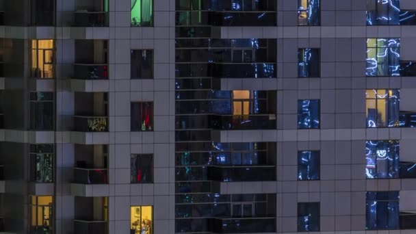 Filas de ventanas brillantes con gente en el edificio de apartamentos por la noche . — Vídeo de stock