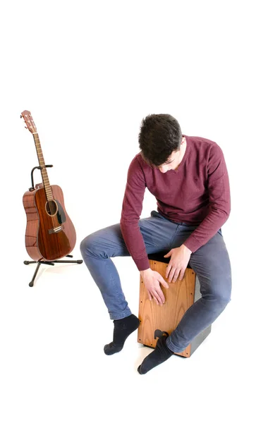 Muzyk mężczyzna nastolatek siedzieć na cajon i grać z gitarą w b Obrazek Stockowy