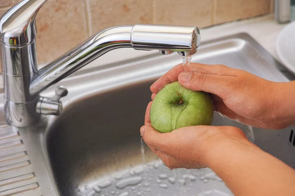 Kvinna som tvättar ett äpple med vatten i diskhon — Stockfoto