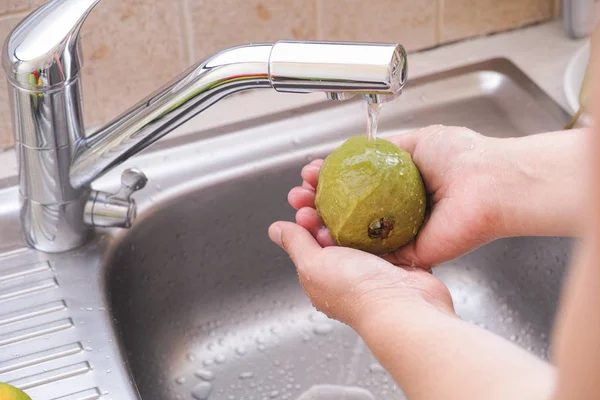 Kvinna som tvättar en guava med vatten i diskhon — Stockfoto