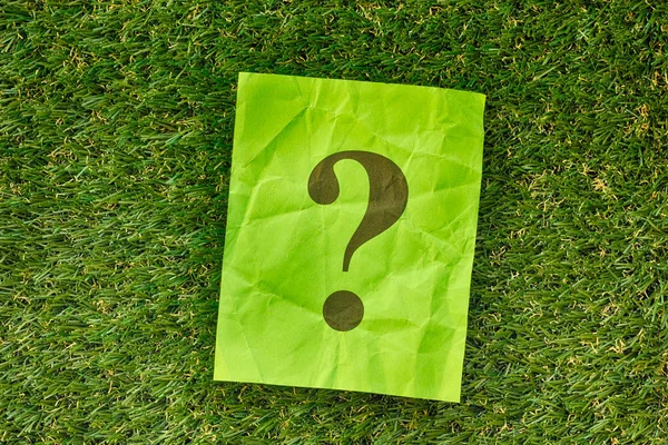 Paper note with question mark on green grass